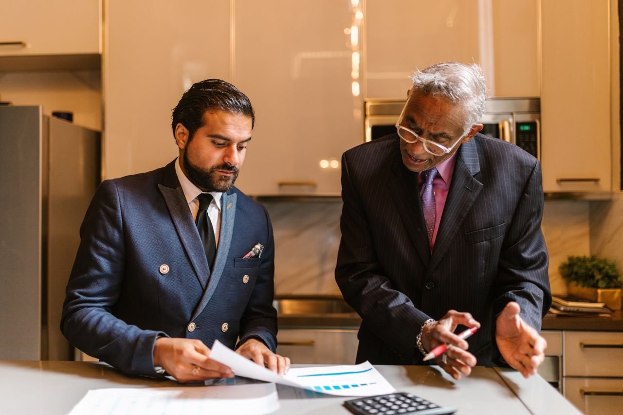 About Two businessmen engaged in a focused discussion over financial documents in a modern office setting.